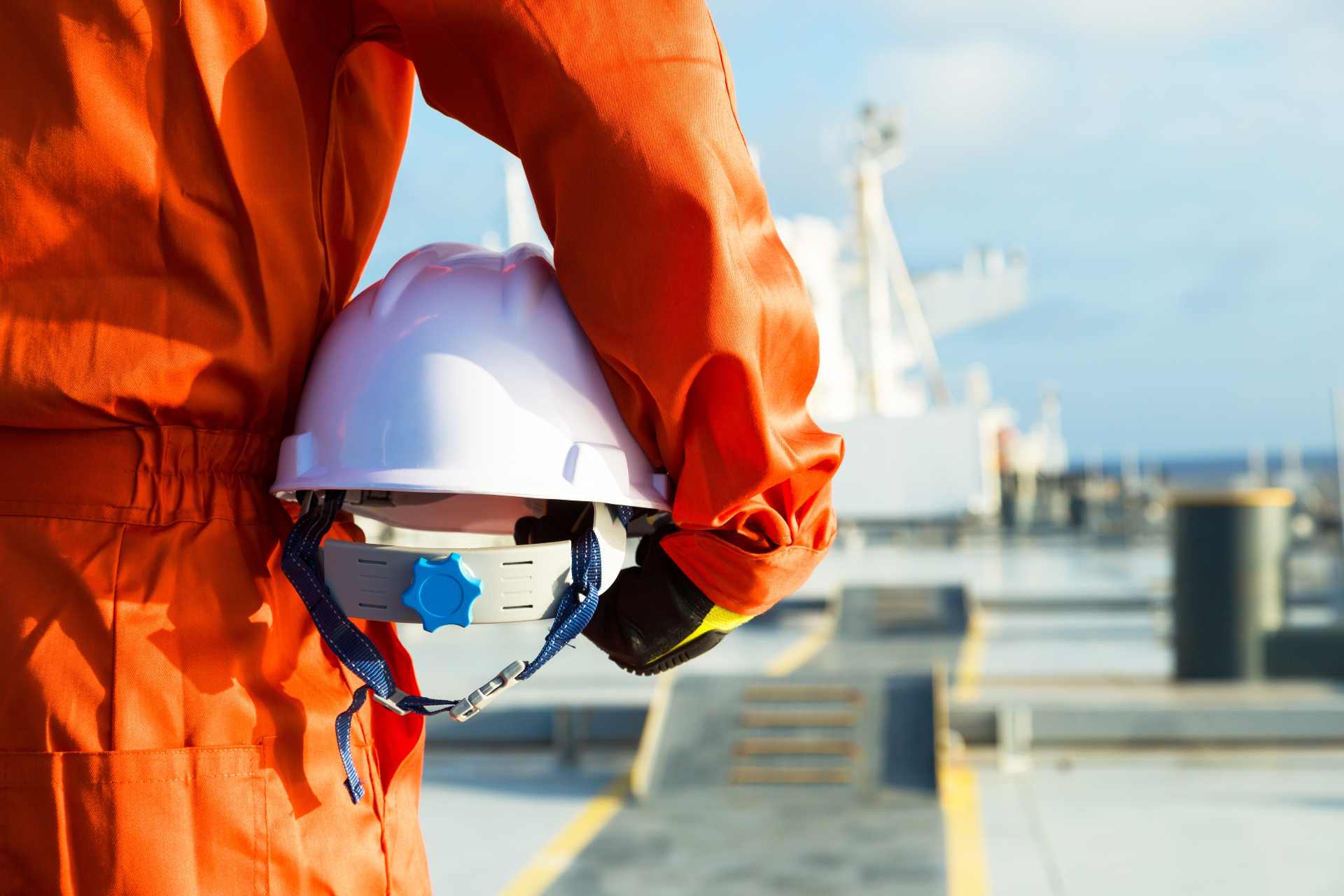 Picture of a person wearing a safety suit and holding a helmet in their hands while standing on a dock.