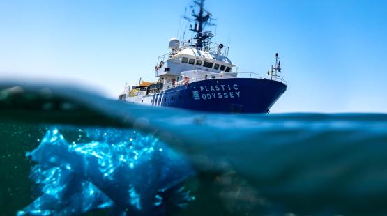 Plastic Odyssey boat at sea, visible waste in the water.