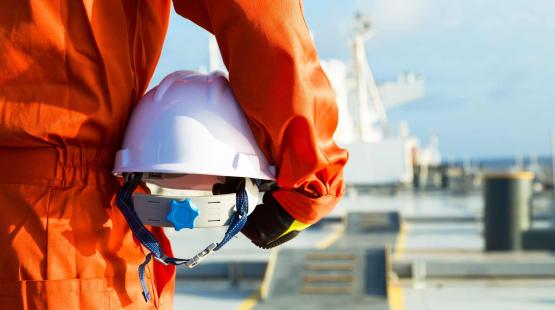 ©Anatoly Menzhiliy - TotalEnergies Picture of a person wearing a safety suit and holding a helmet in their hands while standing on a dock.